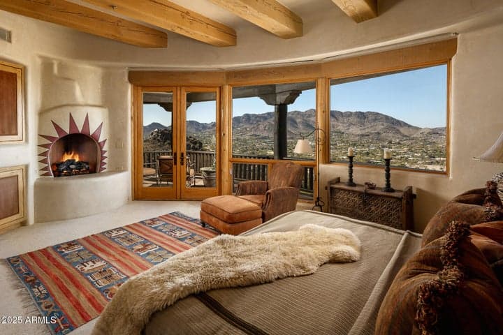 A fireplace adds warmth and ambiance to this spacious primary bedroom, which boasts panoramic windows, mountain views, and private patio access. A peaceful setting for relaxation in an architecturally significant estate.