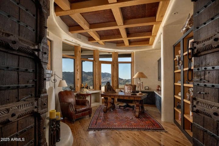 A richly appointed office with panoramic windows and a private patio creates the perfect work-from-home setting. Custom coffered ceiling, warm wood finishes, and mountain views add prestige to this refined space.
