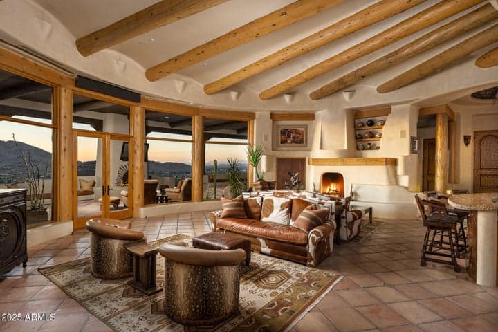 This luxurious living area blends rustic charm and elegance with a large kiva-style fireplace, exposed wood beams, and curved architecture. The open design allows for easy flow between indoor and outdoor spaces, maximizing comfort and visual appeal.