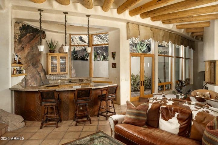 This spacious great room offers luxurious comfort with a built-in wet bar featuring natural stone accents and custom cabinetry. Large windows overlook a tranquil Zen garden, bringing serene desert landscaping indoors. Perfect for hosting in style in your Paradise Valley estate.