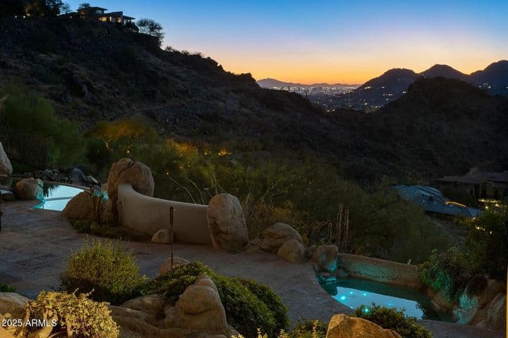 Nestled against the hillside, this resort-style yard offers a glowing spa and pool set amidst natural boulders and mature desert landscaping—ideal for relaxing or entertaining with stunning nighttime ambiance.