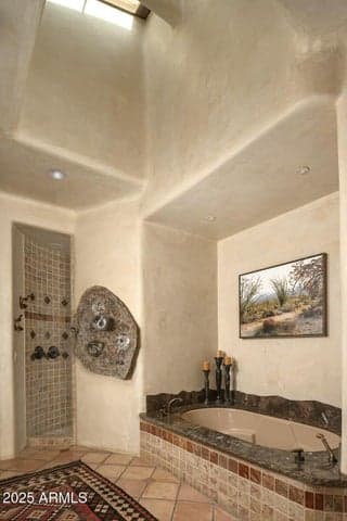 Relax in the stunning primary bath complete with a deep soaking tub, natural stone finishes, and a custom rain shower set into a tile alcove. Vaulted ceilings and rich textures enhance the spa-like atmosphere of this upscale Paradise Valley home.