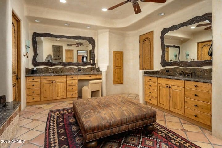 This spacious primary bathroom in Paradise Valley offers dual vanities with granite countertops, custom wood cabinetry, and unique framed mirrors. The layout emphasizes luxury and functionality with separate prep areas and warm natural tones, making it the perfect private retreat