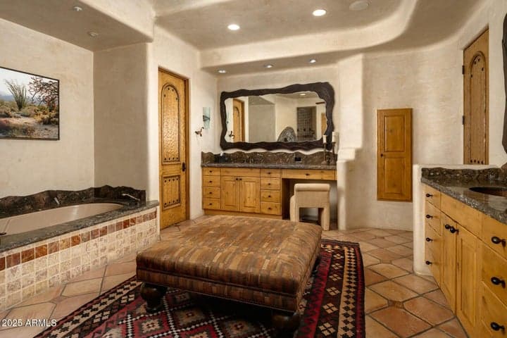 Unwind in this spa-inspired primary bathroom featuring dual vanities, a built-in makeup counter, and a luxurious soaking tub with stone surround. Southwestern design meets comfort in this beautifully appointed space within an elegant Arizona estate.