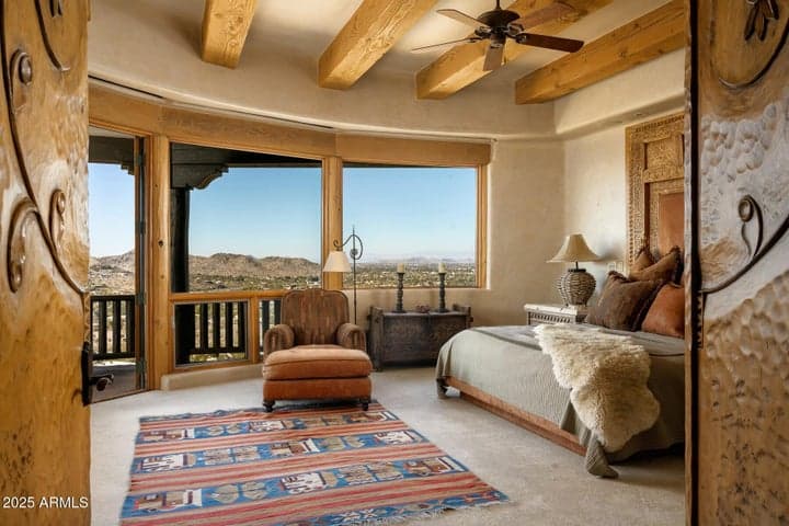 Enter the primary suite through hand-carved double doors and experience unobstructed views across the valley. Natural wood elements and ambient light enhance the spacious comfort and southwestern elegance of this room.